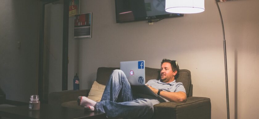 man lying on couch while using laptop computer