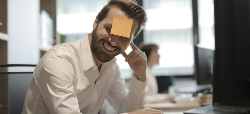 Man having fun with a sticky note on forehead in a modern office setting.